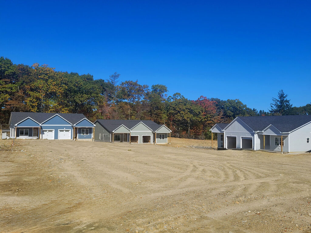 Row of newly built homes under construction at Harmony Place in Rutland, Massachusetts, with a clear blue sky overhead.