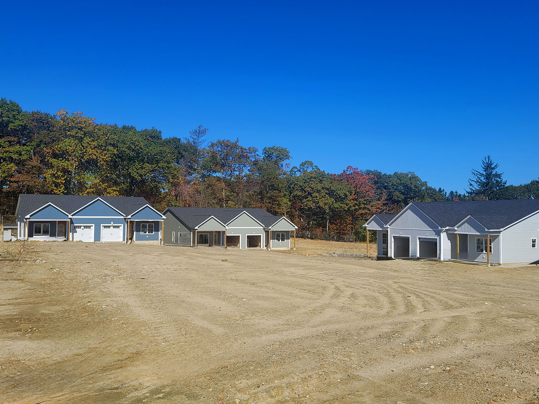Row of newly built homes under construction at Harmony Place in Rutland, Massachusetts, with a clear blue sky overhead.