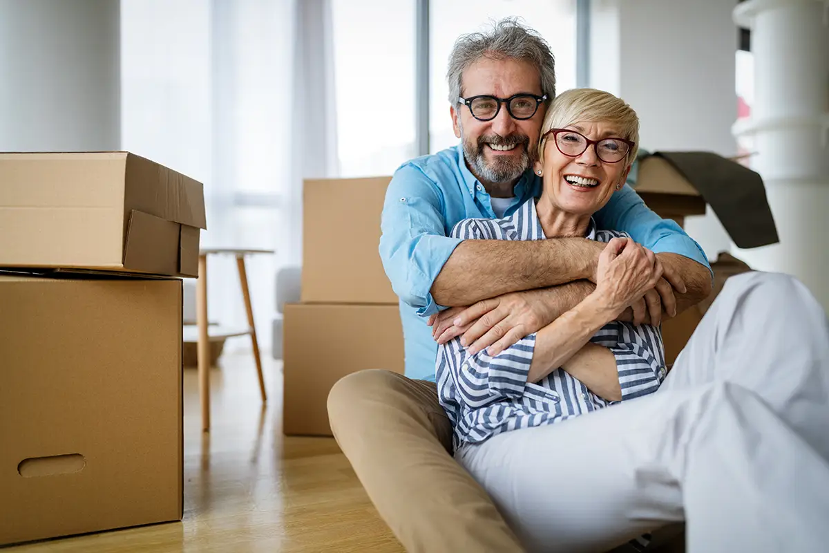 Happy senior couple surrounded by moving boxes in their new home, representing downsizing and storage space in a 55+ community.